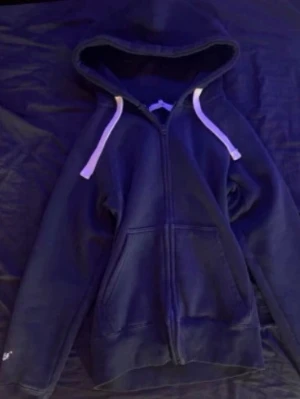 Mörkblå zip hoodie med vita snören russemerch  - Mörkblå hoodie med dragkedja och vita snören i huvan. Tröjan har två stora fickor framtill och ribbade muddar vid ärmslut och nederkant. Perfekt för en avslappnad och sportig stil. använd 2-3 gånger inga defekter eller hål