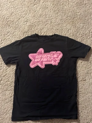 Svart t-shirt med World wide märket  - Säljer en svart t-shirt med ett stort rosa stjärntryck och texten 'world wide' på bröstet. T-shirten har klassisk passform och korta ärmar. Perfekt för dig som gillar streetwear vibes och vill sticka ut lite extra.