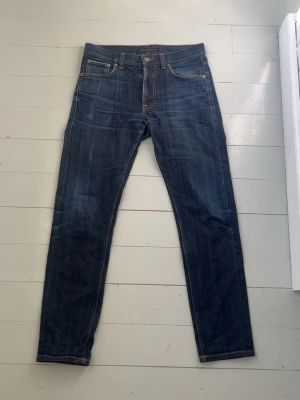 Nudie Jeans Lean Dean Selvedge – W31 L32 - Säljer ett par mörkblå jeans från Nudie med smal passform och klassiska fem fickor. Jeansen har kontrastsömmar och Nudie-logga på bakfickan. Tillverkade i denim med snygg tvätt och raka ben. Perfekta för en stilren vardagslook.