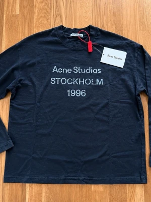 Acne Studios långärmad - Snygg svart långärmad topp från Acne Studios med tryck 'Acne Studios STOCKHOLM 1996' framtill. Klassisk passform och rund hals. Perfekt till jeans eller kjol för en clean och trendig look.
