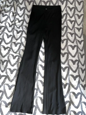 Ribbade tights  - Säljer ett par svarta ribbade byxor med utsvängda ben. Byxorna har hög midja och ett mjukt, stretchigt material som ger en snygg passform. Perfekta för dej som gillar en trendig och bekväm stil. Det finns en obehandlade liten fläck.