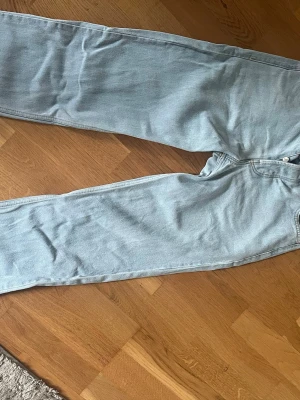 Ljusblå raka jeans - Säljer ett par ljusblå jeans med rak passform och klassisk femficksdesign. Jeansen har bälteshällor och knappgylf. Materialet är denim i bomull och färgen är riktigt fräsch ljusblå, perfekt till en avslappnad look.