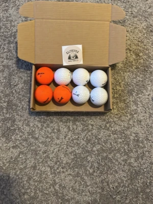 Srixon mix A/B klass - Säljer ett set med åtta golfbollar i en kartong, fyra är vita och fyra är orange. Bollarna har olika tryck och märken, och kommer i en praktisk förpackning från Elitetee Golf Balls. Perfekt för dig som vill ha variation på golfbanan.