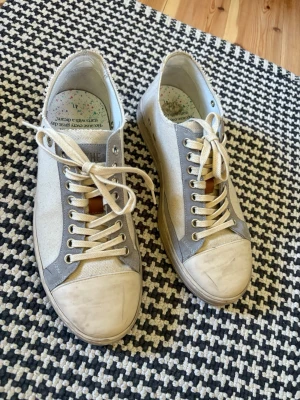 The Gallerist skor strl 41, använda 3 ggr - Snygga låga sneakers i vitt och ljusgrått tyg med vita snören och detaljer i läderimitation. Skorna har en klassisk rund tå och metallöljetter för snörningen. Perfekta för en avslappnad och trendig stil.