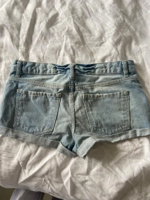 Super snygga lågmidjade jeansshorts  - Säljer ett par ljusblå denimshorts med uppvikta benslut och klassisk femficksdesign. Shortsen har bälteshällor och stängs med knapp och dragkedja. Perfekta för varma dagar och enkel att matcha med olika toppar.