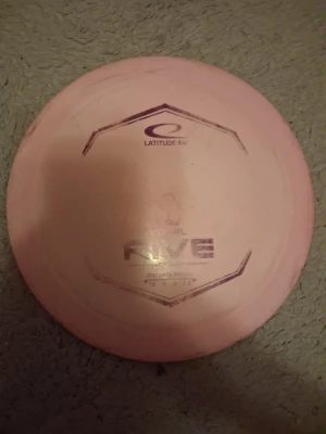 Rosa discgolf disc Latitude 64 Rive - Säljer en rosa discgolf disc av modellen Rive från Latitude 64. Discen är rund med tryckt logga och text på ovansidan. Perfekt för dig som gillar discgolf och vill ha en stabil distance driver i samlingen. Kan pruta lite om man vill! Och disc statsen är 13 speed 5 glide 0 turn 3.5 fade.