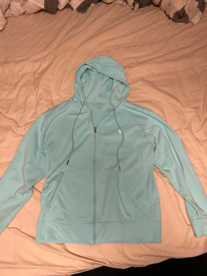 Ljusblå hoodie från Polo Ralph Lauren - Snygg ljusblå hoodie från Polo Ralph Lauren med dragkedja framtill, två fickor och justerbar huva med snören. Tillverkad i mjukt bomullsmaterial och har den klassiska Polo-loggan broderad på bröstet. Perfekt för en avslappnad och stilren look.