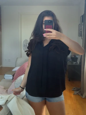 Svart ärmlös blus med knyt - Säljer en svart ärmlös topp med lös passform och v-ringad hals. Toppen har en enkel och clean design utan synliga detaljer köpt för 350kr💞