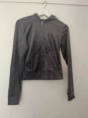 Mjuk grå velour hoodie - Säljer en stilren grå hoodie i mjuk velour med dragkedja framtill. Tröjan har huva och långa ärmar, perfekt för en chill och avslappnad look. Passar dig som gillar bekväma och trendiga plagg. Endast använd en gång så i väldigt fint skick.