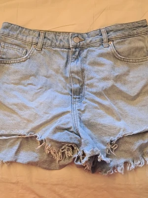 Ljusblå vintage jeansshorts från clockhouse - Ljusblå denimshorts med fransig, rå kant och klassisk femficksmodell. Shortsen är o storlek 42, men passar mindre - Speciellt om man vill ha den low waist, då är det perfekt om man brukar ha mindre storlek än 42!  Köpta i London på en vintage butik! Super bra skick! Använda 2 gånger. 
