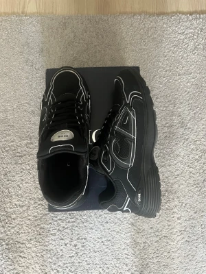 Svarta  sneakers med vita detaljer - Snygga svarta sneakers  med vita kontrastsömmar och CD-logga i silver på hälen. Skorna har en chunky sula, meshpaneler och klassisk snörning. Perfekta för dig som vill ha en exklusiv och trendig look.