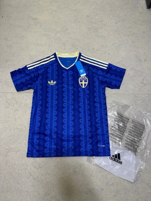 Blå Sverige fotbollströja Adidas - Tröjan är helt ny och oanvänd, i nyskick. Den är väldigt bekväm att ha på sig och har en stilren design utan namn eller nummer på ryggen, vilket gör den perfekt för dig som vill ha en klassisk supportertröja.  Information:  * 🇸🇪 Sverige VM 2026-tröja * Färg: Blå * Storlek: S * Helt ny och oanvänd * Ingen spelare eller nummer på ryggen * Mycket bekväm passform  Skickas eller hämtas enligt överenskommelse. Hör gärna av dig vid frågor!