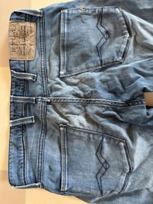 Ljusblå jeans från Replay - Säljer ett par ljusblå jeans från Replay med klassisk femficksmodell och snygga detaljer på bakfickorna. Jeansen har ett hål i ena benet och lite slitningar runt om där av priset 🟩