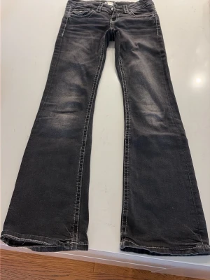 Grå bootcut jeans med slitningar - Snygga grå bootcut jeans med lätt slitna detaljer och kontrastsömmar. Jeansen har klassisk femficksdesign och bakfickor med lock och knapp. Perfekta för en avslappnad och trendig look. Storlek 146. 