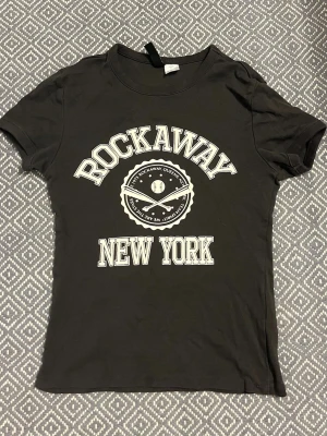 Svart t-shirt med tryck - Snygg svart/mörkgrå t-shirt med vit text och tryck framtill. T-shirten är gjord i 100% bomull, perfekt till jeans eller shorts.