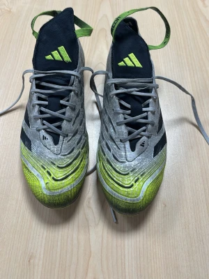 Adidas Predator fotbollsskor grå/gul - Säljer ett par Adidas Predator fotbollsskor i grått och neongult med svarta detaljer. Skorna har snörning, låg profil och mönstrad ovandel för bättre bollkontroll. Perfekta för dig som vill sticka ut på planen och få grym touch på bollen.