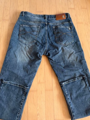 Blå jeans från Brunello Cucinelli - Säljer ett par blå jeans från Brunello Cucinelli med raka ben och dubbla bakfickor. Jeansen har slitningar och kontrastsömmar samt detaljerade sömmar på benen. Klassisk femficksmodell i denim med logotyp på linningen.