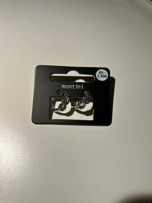 Silverfärgade örhängen från Montini - Snygga silverfärgade örhängen från Montini med kedjedetaljer. Örhängena är små hoops med en cool, chunky design som ger en trendig vibe. Perfekta för att lyfta din stil med en modern touch. Oanvända.