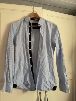 Blåvit randig skjorta Savvy Citizen - Snygg blåvit randig skjorta från Savvy Citizen i storlek Small. Skjortan har långa ärmar, klassisk krage och vita knappar. Tillverkad i bomull och passar perfekt till en stilren look.