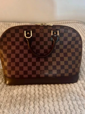 Louis Vuitton Alma PM Damier Ebene - Säljer en vacker Louis Vuitton Alma PM i Damier Ebene. En klassisk och tidlös modell. Skick: Utsidan är i väldigt fint skick. Dragkedjorna har normalt slitage. Insidan har några små vita fläckar (liknar nagellack) som fanns när jag köpte väskan och som jag inte lyckats få bort. Det lilla låset saknas. • Bredd: 30,4 cm • Höjd: 22,8 cm • Djup: 17,7 cm Serienummer: FL0034 Se gärna bilderna noggrant för skicket. Hör av dig om du har några frågor eller vill ha fler bilder. 🌸