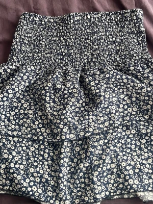 Blommig kortkjol  - Supersöt kortkjol i mörkblått med vitt blommönster och är gjord av ett luftigt material, perfekt för varmare dagar.