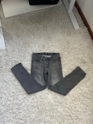 Grå skinny jeans med stretch - Säljer ett par grå skinny jeans med hög midja och klassisk femficksdesign. Jeansen har en snygg tvättad look och är tillverkade i ett stretchigt material som sitter tajt längs benen. Perfekta för dig som gillar en smal siluett och vill ha ett par stilrena jeans.