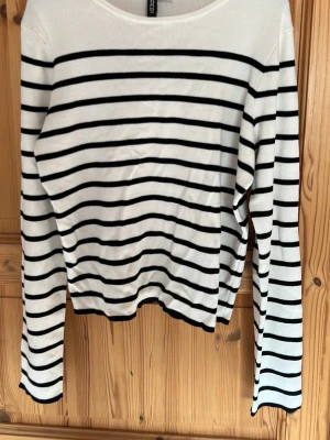 Vit långärmad tröja med svarta ränder - Snygg vit långärmad tröja med svarta horisontella ränder. Tröjan har rund halsringning och är i ett mjukt, tunt material som passar perfekt till jeans eller kjol. Enkel och stilren design som funkar året runt.