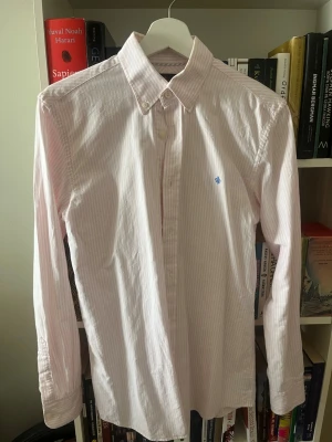 Rosa och vit randig skjorta Morris XS - Snygg rosa och vit randig skjorta från Morris i storlek XS. Skjortan har klassisk krage med knappar, lång ärm och diskret broderad logga på bröstet. Tillverkad i mjuk bomull för en bekväm känsla.