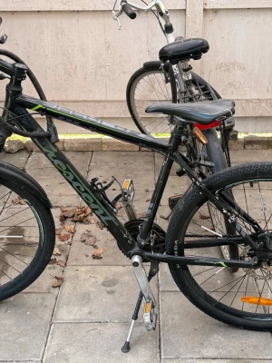 Svart mountainbike med gröna detaljer - Säljer en svart mountainbike med gröna och grå detaljer. Cykeln har breda däck, skivbromsar, stänkskärmar och ett stabilt styre. Perfekt för dig som vill ha en cykel för både stad och terräng. Utrustad med stöd och reflexer. Däcken är lite slitna 