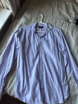 Ljuslila skjorta från Riley slim fit - OBS använd 4 gången! Säljer en stilren ljuslila skjorta från Riley i slim fit-modell. Skjortan har klassisk krage, långa ärmar och knäppning framtill. Perfekt för dig som gillar en enkel men snygg look.