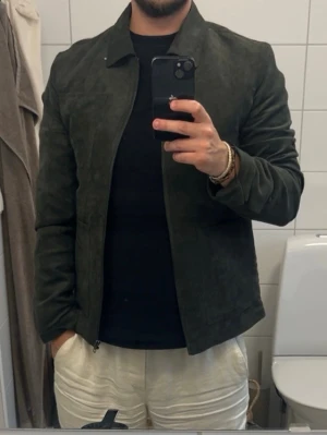 Mörkgrön mockajacka med dragkedja - Stilren mörkgrön overshirt med klassisk krage och dragkedja framtill. Jackan har raka ärmar. Materialet ser ut som mockaimitation vilket ger en lyxig känsla och passar perfekt till en trendig look. Storlek small. Aldrig använd.