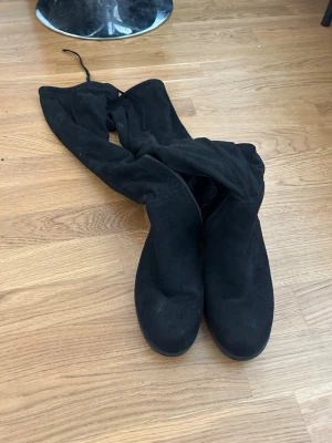 Svarta overknee stövlar i mockaimitation - Säljer ett par svarta overknee stövlar i mjuk mockaimitation. De har rund tå, låg klack och snörning upptill för att sitta snyggt på benet. Dragkedja på insidan för enkel på- och avtagning. Perfekta till höst- och vinterlooken.