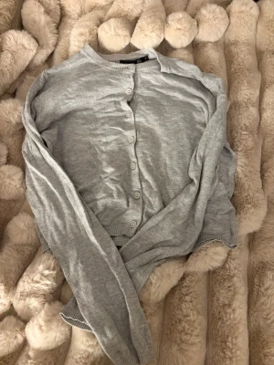 Ljusgrå kofta från 157, storlek M - Ljusgrå kofta med rund halsringning och knäppning framtill från 157. Koftan har långa ärmar och ribbade muddar vid ärmslut och nederkant. Perfekt att slänga över en t-shirt eller linne för en chill look.