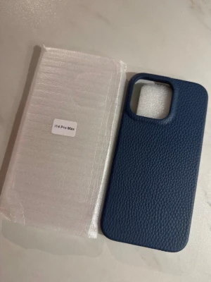 Blått mobilskal i läder till iPhone 14 Pro Max - Nytt!  - Snyggt blått mobilskal med läderstruktur som passar iPhone 14 Pro Max. Skalet har en stilren design med stor öppning för kameran och ger ett bra grepp tack vare den mönstrade ytan. Perfekt för dig som vill ha ett elegant och tåligt skydd till mobilen. Äkta blått Läderskal. 