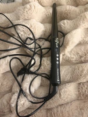 Svart locktång från Remington - Säljer en svart locktång från Remington med smal konformad form och dekorativa blommönster i guld på handtaget. Tången har tre knappar för inställningar och en lång sladd för smidig användning. Perfekt för att fixa snygga lockar snabbt.
