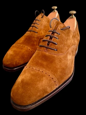 Bruna mockaloafers från Carmina - Snygga loafers i brun mocka från Carmina. Skorna har klassisk design med rundad tå, dekorativ söm över tån och mörkbruna snören. Yttermaterialet är mjukt och lyxigt, perfekt för dig som gillar stilrena och tidlösa skor. Endast provade inomhus. I storlek 10,5 vilket motsvarar 44,5. 