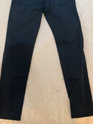 Svarta jeans från Åhléns ANK - Snygga svarta jeans från ANK med klassisk femficksmodell. Jeansen har raka ben och är tillverkade i ett mjukt bomullsmaterial med lite stretch för extra komfort. Perfekta för dig som gillar en stilren och enkel look.