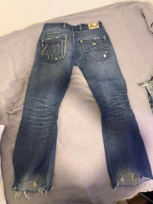 Armani jeans - Snygga blå jeans med slitna detaljer och fransade benslut. Bakfickan har en stor AJ-brodyr i kontrastfärg. Jeansen har klassisk femficksdesign och en cool, avslappnad look. Perfekta för dig som gillar streetstyle och unika detaljer. Sitter som L30