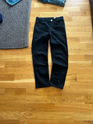 Svarta raka jeans - Svarta jeans med rak passform och klassisk femficksdesign. Jeansen har knapp- och dragkedjegylf samt bälteshällor i midjan. Materialet ser ut att vara denim med lite stretch för extra komfort.
