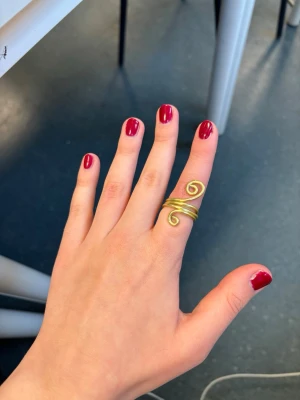 Guldig spiralring i metall - Unik ring i guldtonad metall med spiralformad design. Ringen består av tunn metalltråd som är tvinnade och avslutas i två dekorativa snurror. Perfekt för dig som gillar statement-smycken och vill ha något annorlunda.