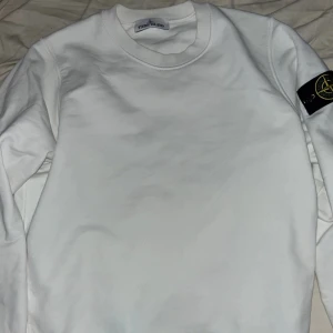 STONE ISLAND Äkta  - Säljer en stilren vit sweatshirt från Stone Island med klassisk patch på vänster ärm. Tröjan har rund halsringning och långa ärmar. Perfekt för en clean och avslappnad look. Kvitto och orderbekräftelse finns. Använd 1 gång