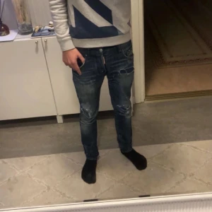 Blå Dsquared2 jeans med slitningar - Säljer ett par blå jeans från Dsquared2 med snygga slitningar och detaljer på benen. Jeansen har slim passform och klassisk femficksdesign. Märkeslapp bak i midjan. Perfekta för dig som gillar streetstyle. Små tecken på användning men allmänt väldigt bra skick. 