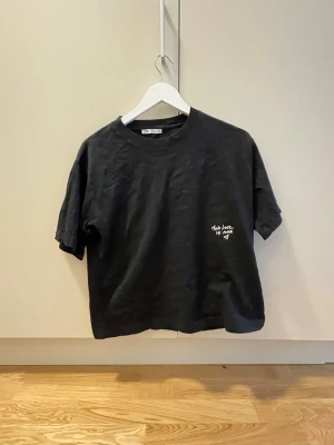 Svart croppad t-shirt med hjärtdetalj - Svart croppad t-shirt med vit text och hjärta på bröstet. Baksidan har en stor hjärtdesign i röda och rosa toner med autografliknande tryck. T-shirten har rund hals och korta ärmar, perfekt för en avslappnad stil.