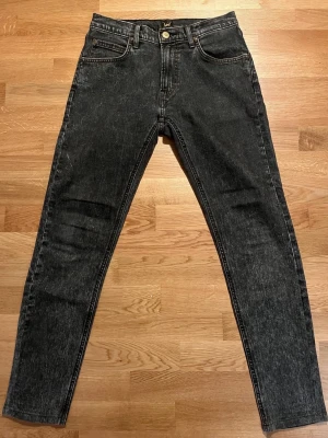 Lee Luke jeans – W30/L31 - Mycket fint skick! - Säljer ett par svarta Lee jeans med smal passform och klassisk femficksdesign. Jeansen har en snygg tvättad look och Lee-läderpatch bak i midjan. Tillverkade i denim med raka ben och dragkedjegylf. Perfekta för en avslappnad och trendig stil.