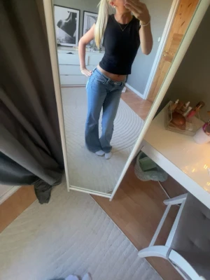 Blå bootcut jeans med nitar - Säljer ett par ljusblå bootcut jeans med snygga detaljer på bakfickorna i form av nitar. Jeansen har låg midja och klassisk femficksdesign. Perfekta för dig som gillar en avslappnad men trendig look.