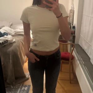 Vit cropped t-shirt med tryck (off-white/cream) - Säljer en vit cropped t-shirt med korta ärmar och rund hals. T-shirten har ett litet tryck nere vid fållen på framsidan. Enkel och clean design som passar till det mesta. Perfekt för dig som gillar en basic men ändå trendig stil. Aldrig använt ock bra kvalitet. 