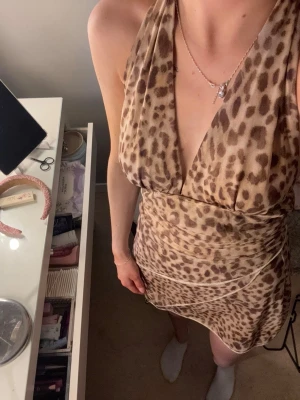 Leopardmönstrad kort klänning - Säljer en snygg leopardmönstrad kort klänning med djup v-ringning och omlottdetalj. Klänningen är ärmlös och har en figurnära passform som framhäver siluetten. Perfekt för dig som vill sticka ut med ett djuriskt mönster.