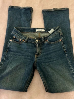 Mörkblå raka jeans från Lindex - Säljer ett par klassiska mörkblå jeans från junkyard  med utsvängda och femficksmodell. Jeansen har snygga kontrastsömmar och kopparfärgade nitar. Tillverkade i slitstark denim med dragkedjegylf och bälteshällor.