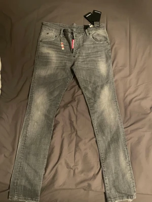 Grå slim fit jeans från Dsquared2 - Snygga grå slim fit jeans från Dsquared2 med slitna detaljer och klassisk femficksdesign. Jeansen har en diskret tvättad look och raka ben. Perfekta för dig som gillar en modern och trendig stil.