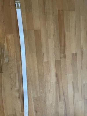 Vitt skärp med guldspänne -  vitt skärp med ett stort, fyrkantigt guldspänne i metall och stilren design. Skärpet är gjort i slätt skinn och har en bred rem som ger en modern look. Perfekt accessoar för att lyfta din outfit.